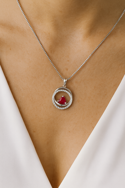 Silver necklace with a red gemstone pendant on a person wearing a white top.